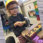 Photo of young white female wearing a safety helmet using a hammer.